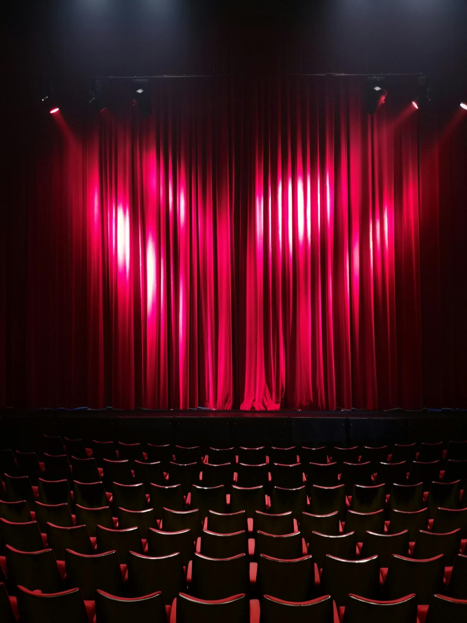 A dramatic scene of red curtains in a theater with empty seats, ready for a performance.